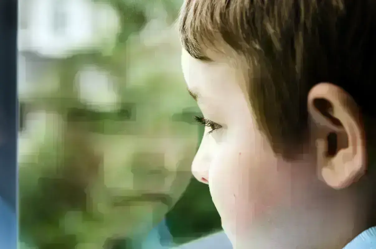 Sad child looking through the window.